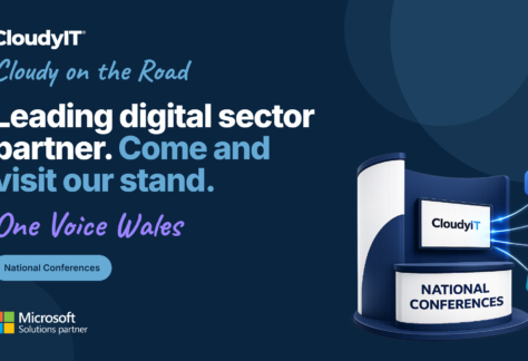 A promotional banner for CloudyIT's presence at the One Voice Wales conference, part of the "Cloudy on the Road" in-person event series. The background is dark navy blue with a vertical light blue bar on the far left that reads "CLOUDYIT EVENTS." On the left, the main headline reads, "Leading digital sector partner. Come and visit our stand." Below this, the event name "One Voice Wales" is written in a purple handwritten-style font. A light blue badge indicates "National Conferences," and a Microsoft Solutions partner logo sits in the bottom left corner. On the right is a 3D illustration of an exhibition stand. The stand features a screen displaying the CloudyIT logo and a front counter that reads "NATIONAL CONFERENCES." Glowing digital lines connect the screen to four floating 3D icons: a speech bubble, a handshake, a laptop, and a presentation whiteboard.